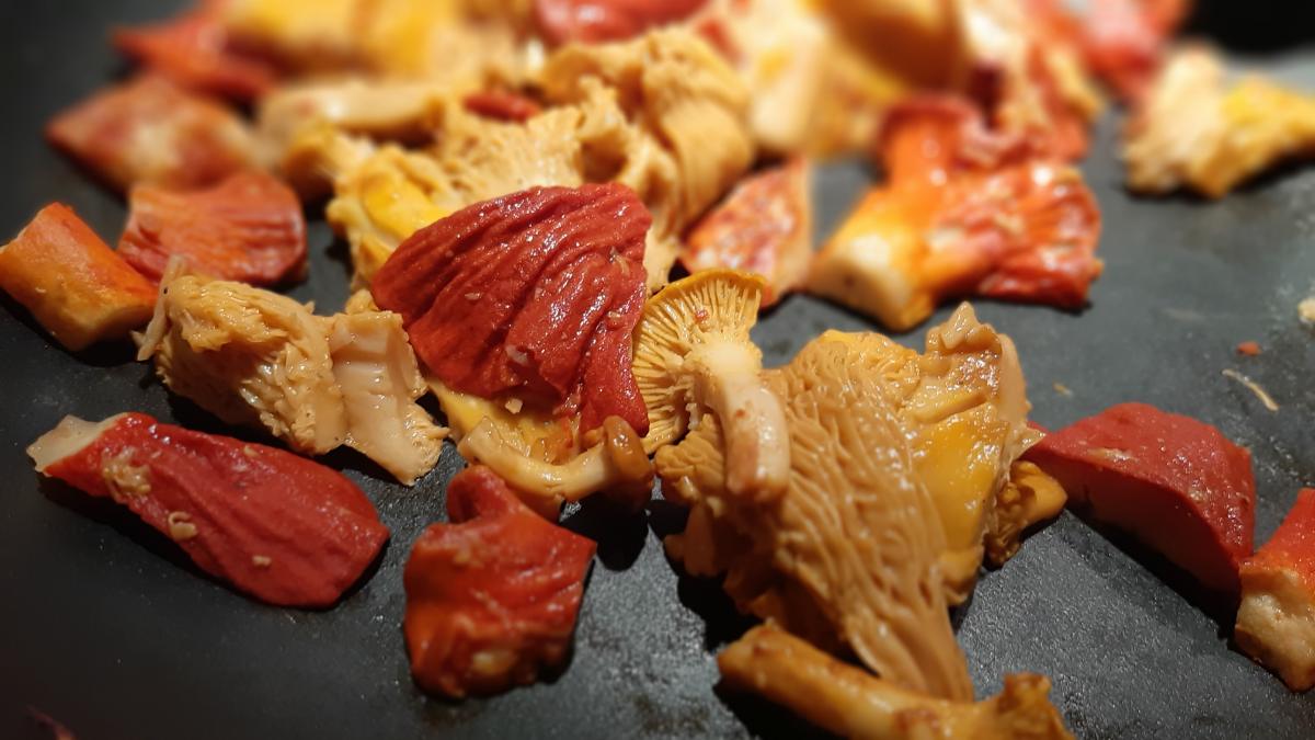Lobster mushrooms being cooked in a pan with chanterelles